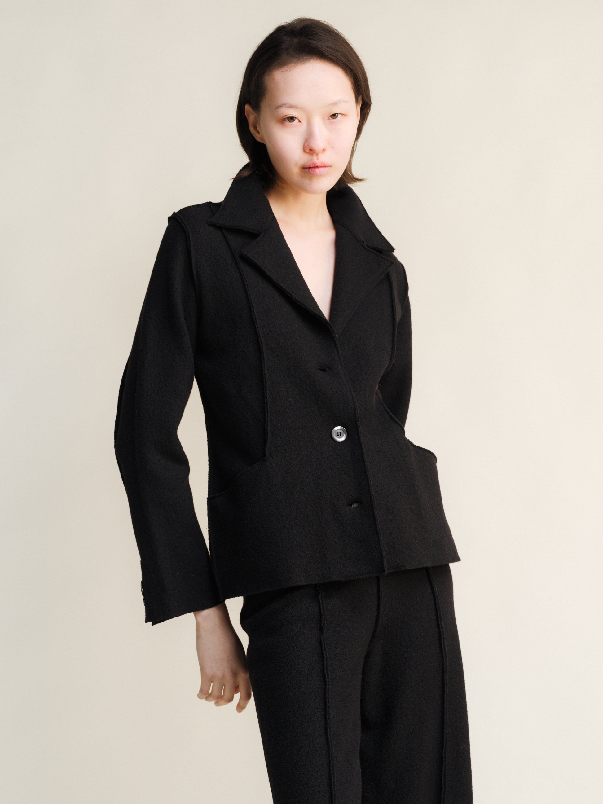 Woman wearing a black boiled wool suit against a plain background