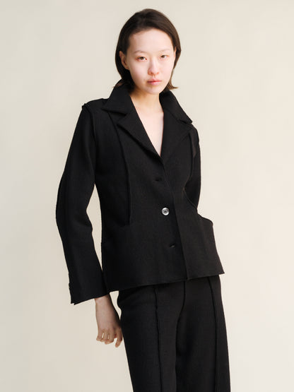 Woman wearing a black boiled wool suit against a plain background
