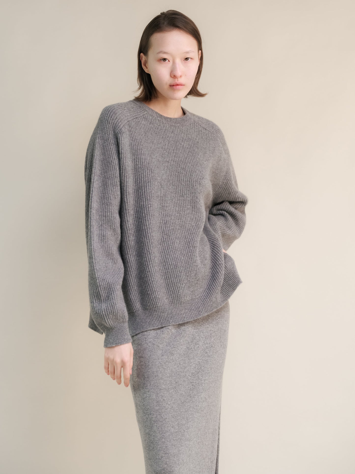 Model wearing gray ribbed cashmere mix crewneck sweater with relaxed fit and a matching knit skirt.