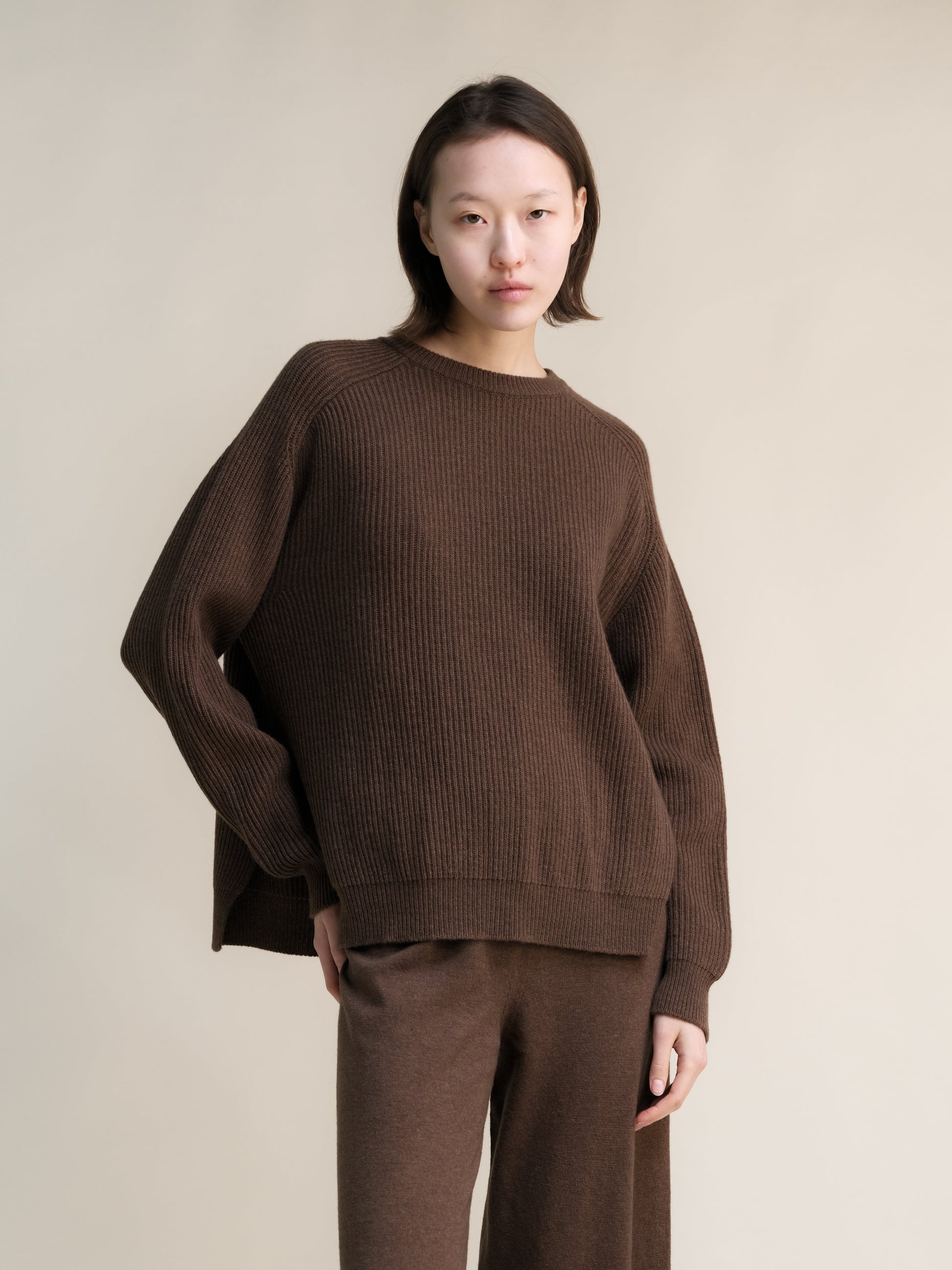 Model wearing a brown ribbed cashmere mix crewneck sweater with lateral slits and matching knit pants