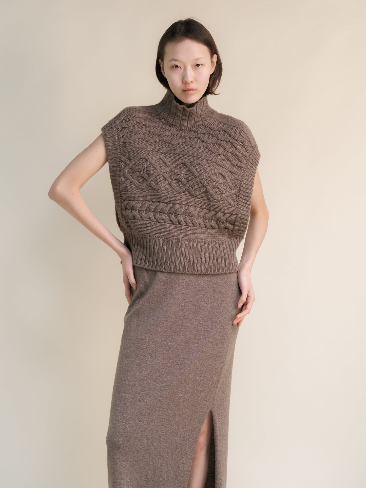 Taupe cashmere mix maxi cable tunic styled as a sleeveless high neck poncho with intricate knit patterns and side openings.