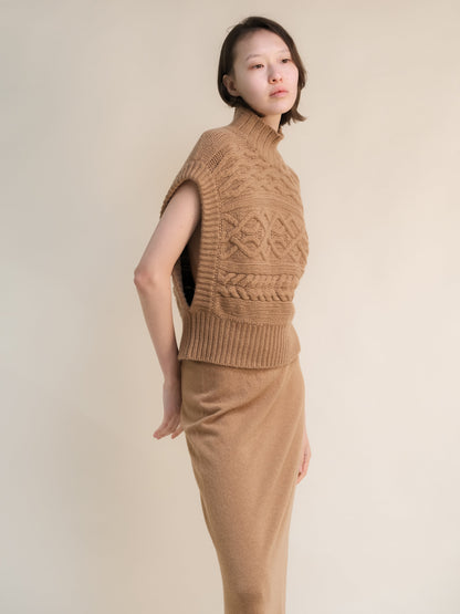 Profile view of a model wearing a tan cashmere mix maxi cable tunic with a high ribbed neck and bold knit patterns.