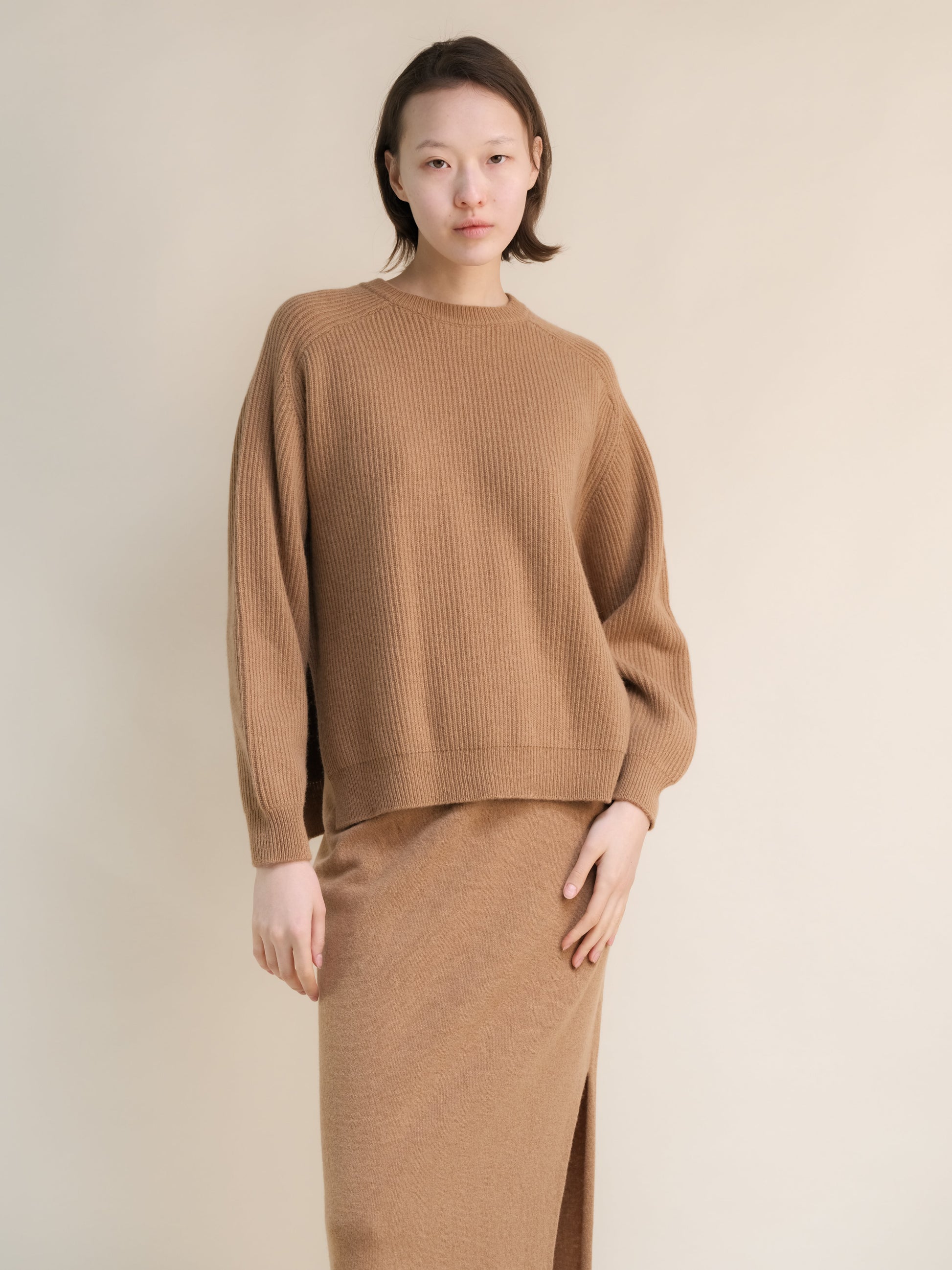 Model wearing camel ribbed cashmere mix crewneck sweater with relaxed silhouette and a matching long skirt.