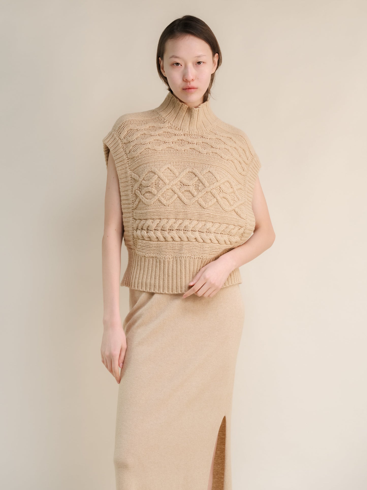 Beige sleeveless cashmere mix maxi cable tunic on a model with a chunky knit pattern and ribbed hem.
