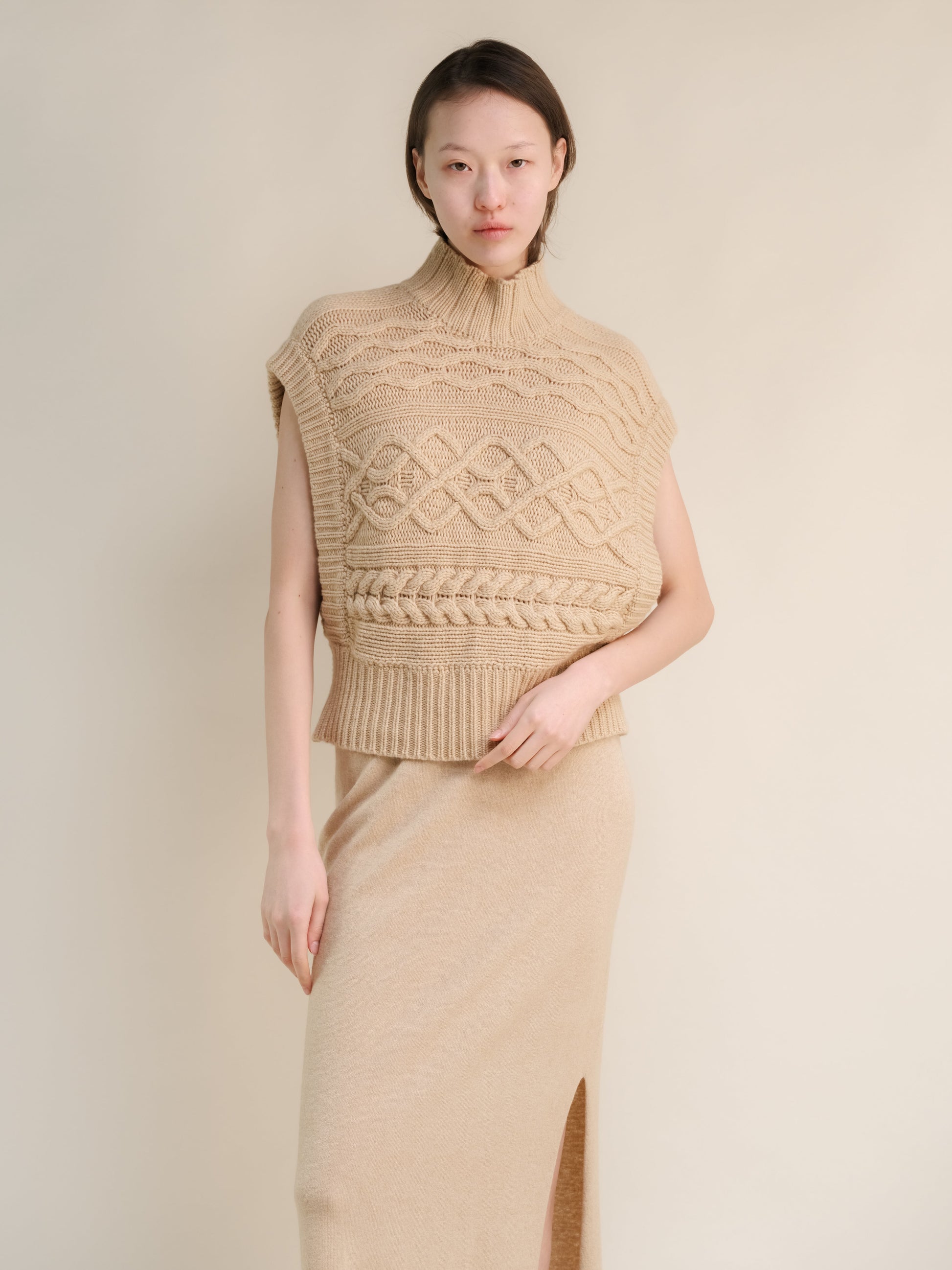 Beige sleeveless cashmere mix maxi cable tunic on a model with a chunky knit pattern and ribbed hem.