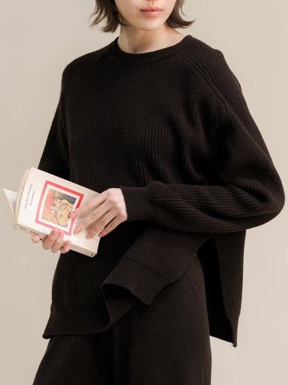 Model wearing black ribbed cashmere mix crewneck sweater with lateral side slits while holding a book