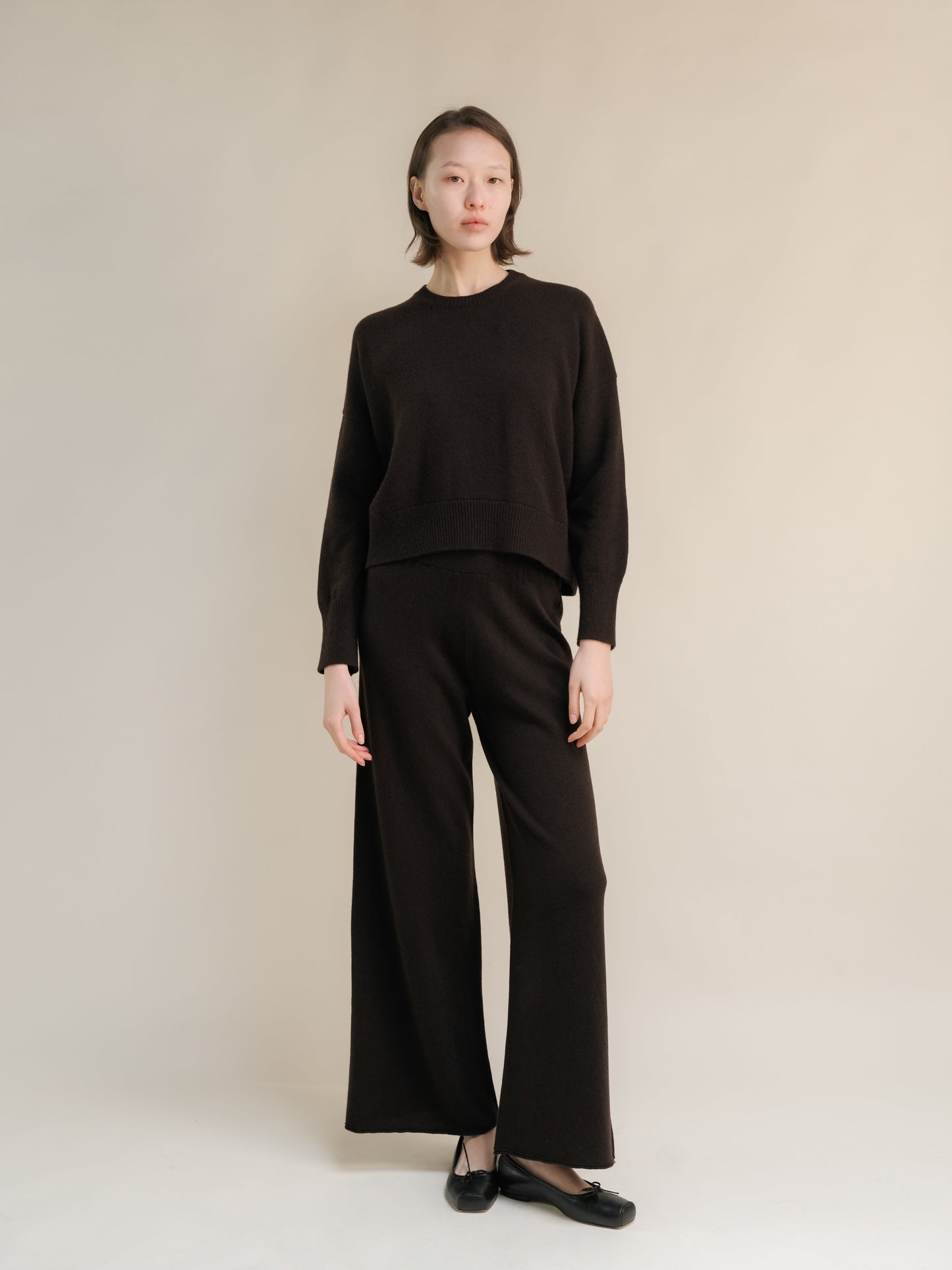 Full-length shot of a model in a dark brown cashmere mix crewneck sweater with matching wide-leg pants.