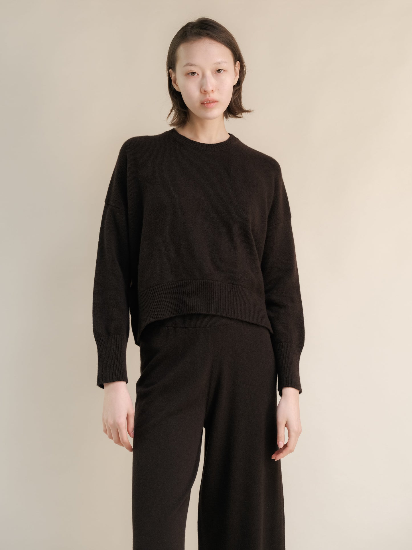 Model wearing a dark brown cashmere mix crewneck sweater with matching wide-leg pants.