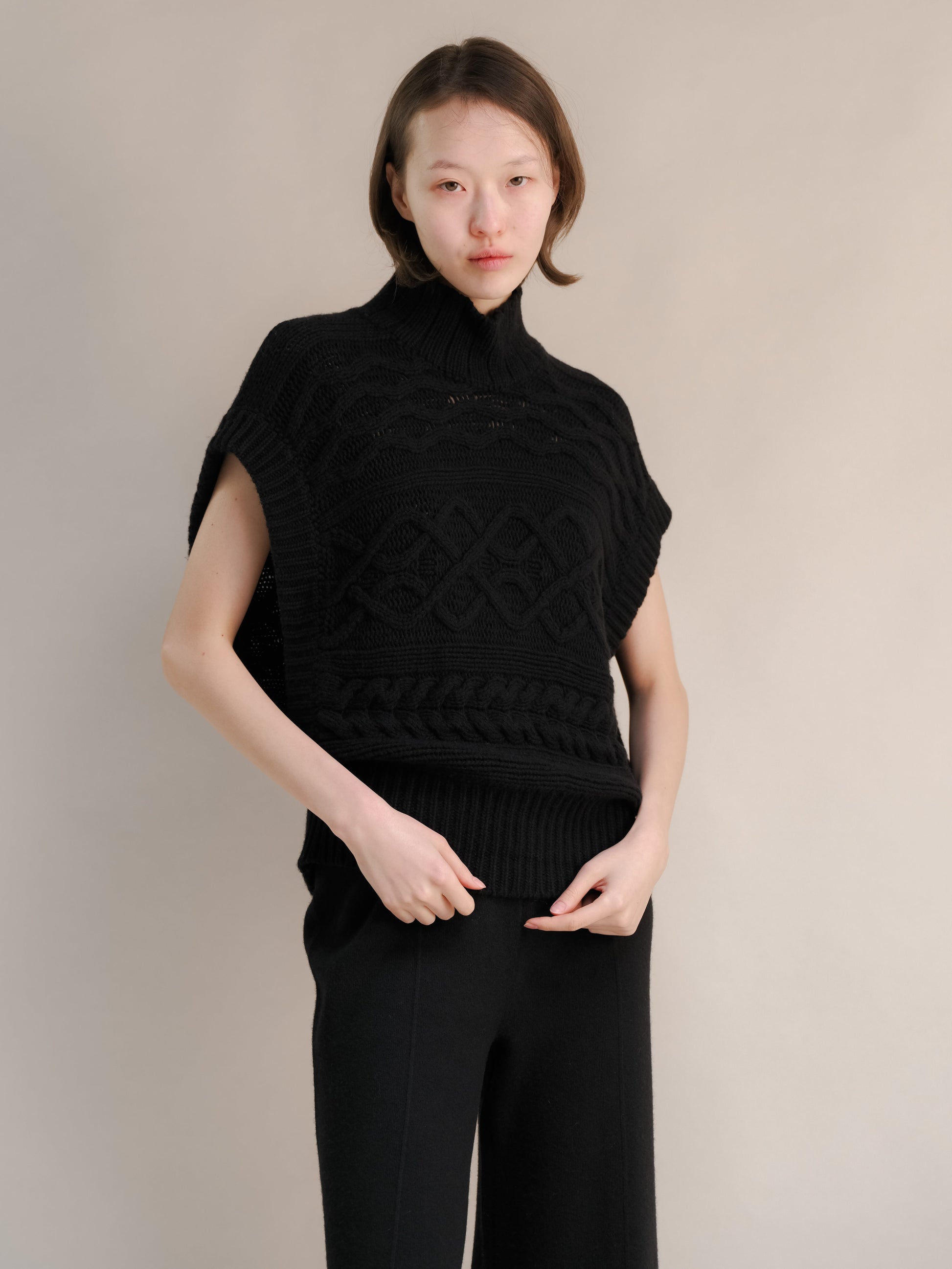 Model wearing a black cashmere mix maxi cable tunic with a snug high neck and chunky cable patterns.