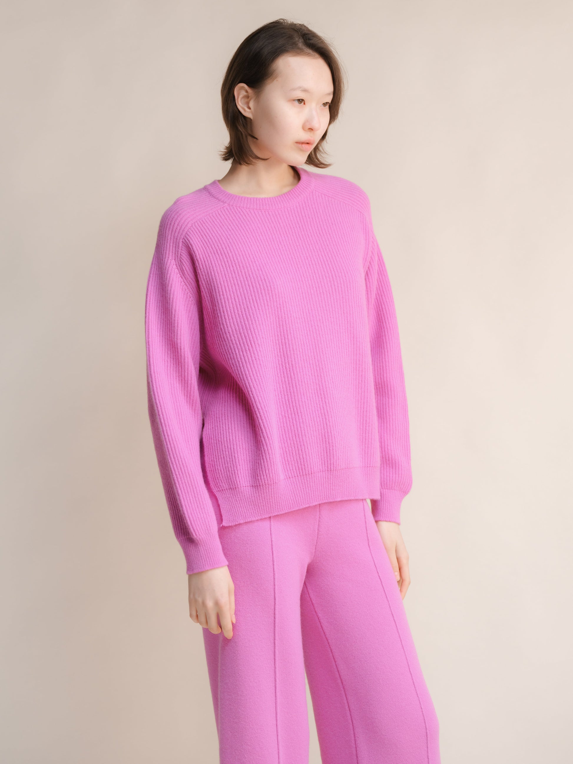 Model wearing a pink cashmere mix crewneck ribbed sweater with side slits and matching pink pants