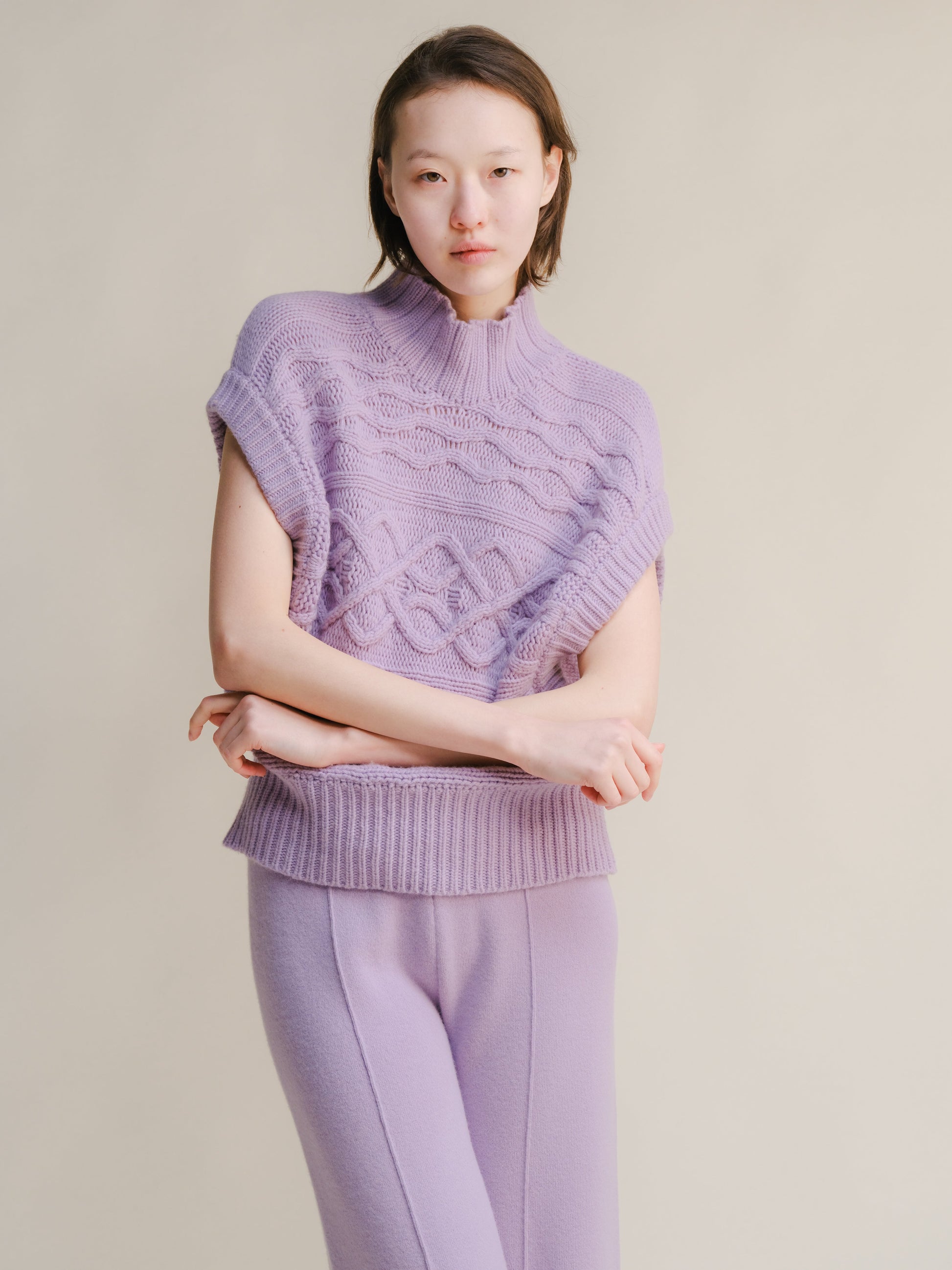 Lilac chunky knit sleeveless tunic with a high neck and cable pattern worn with matching lilac pants.