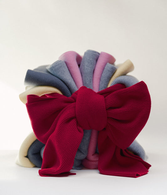 Stack of colorful casmere scarves with one tied in a large red bow on a white background