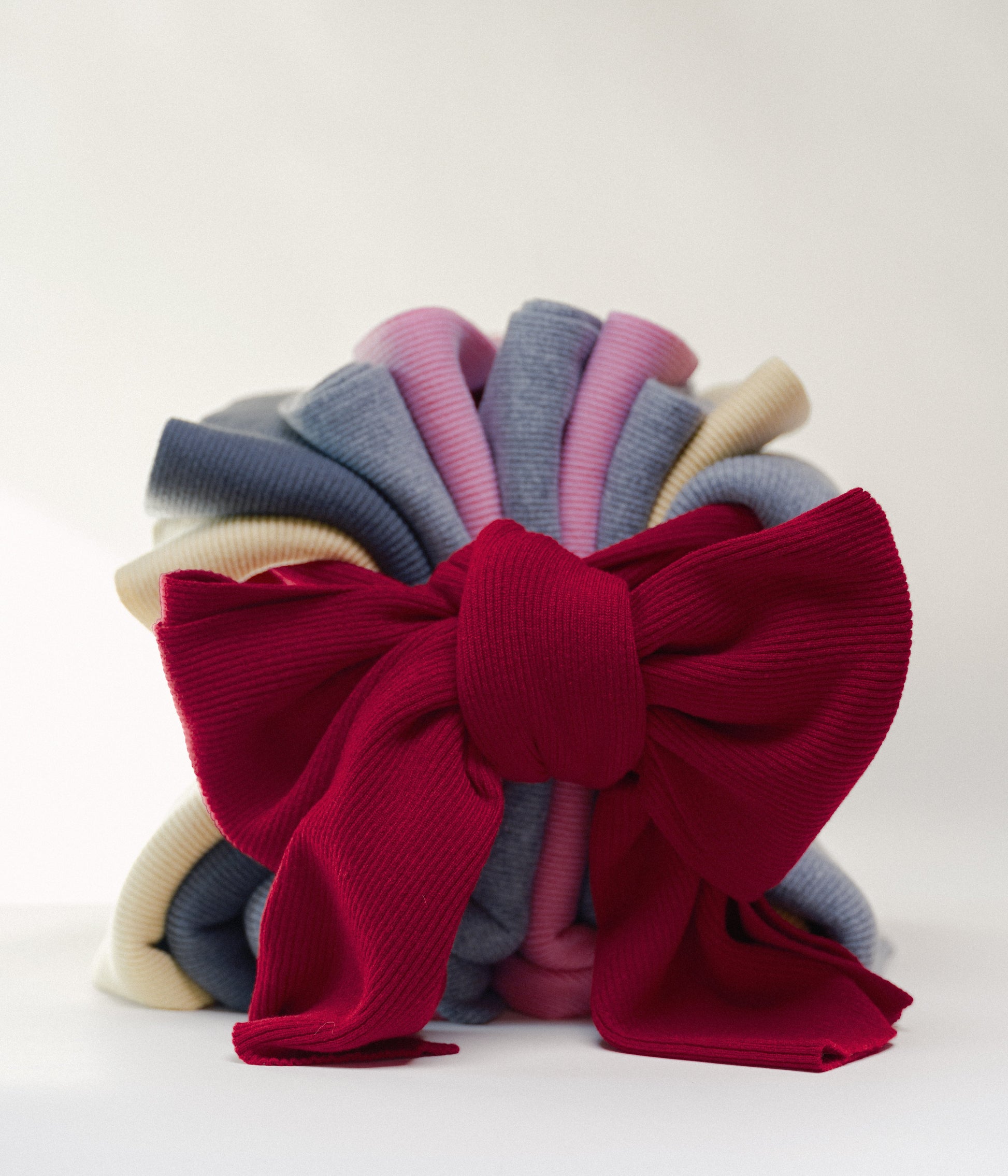 Stack of colorful casmere scarves with one tied in a large red bow on a white background
