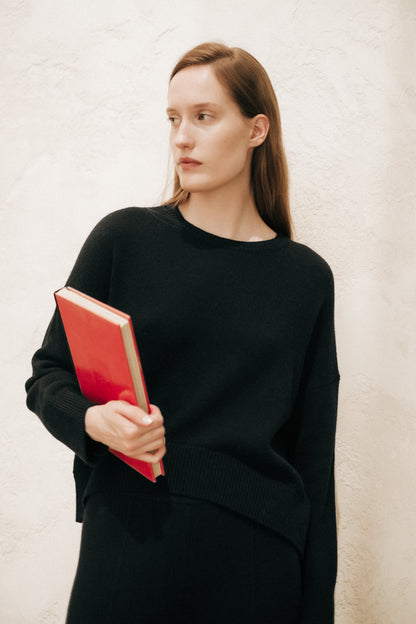 Model in a black cashmere mix crewneck sweater holding a red book.