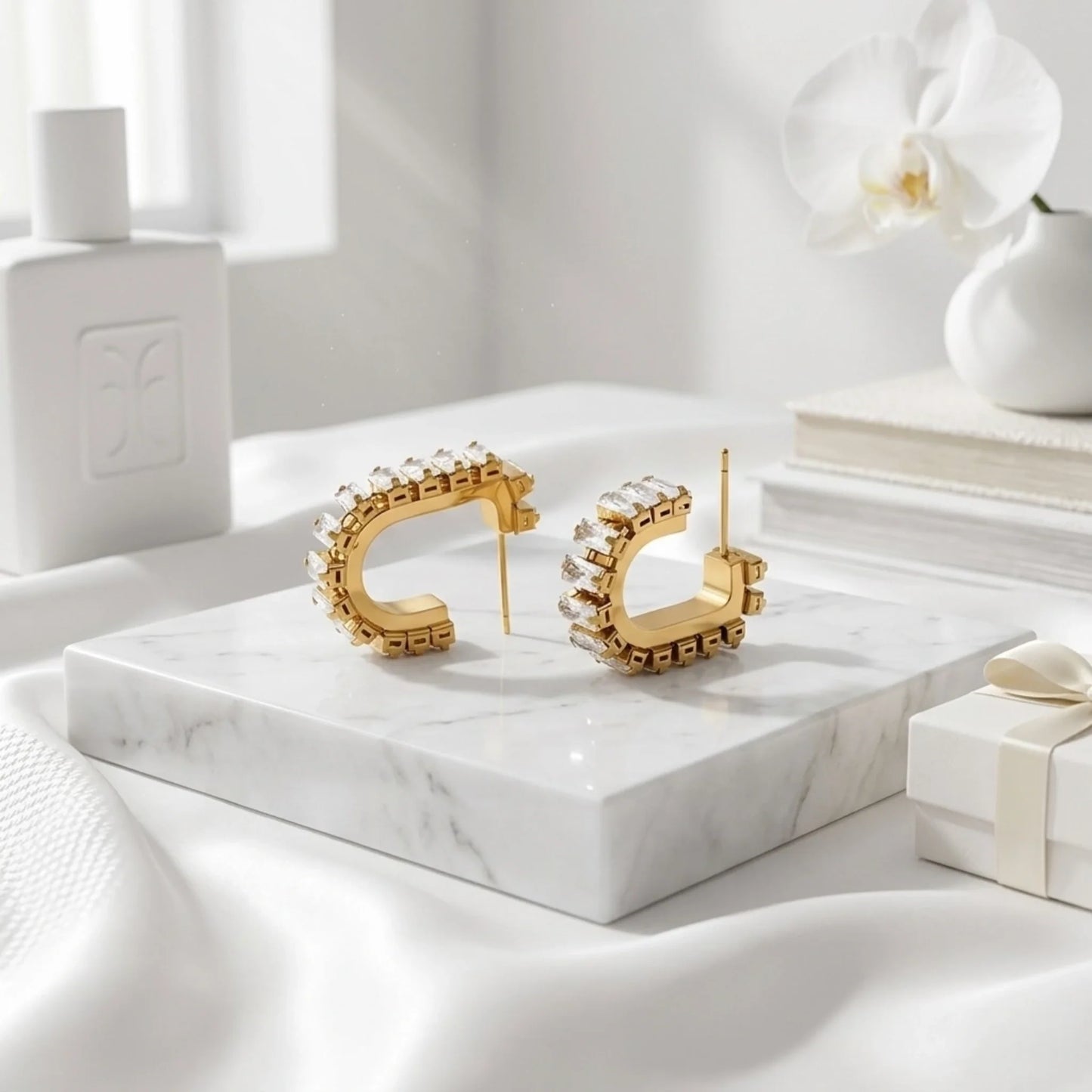 Gold hoop earrings on a marble surface with a white orchid and gift box in the background.