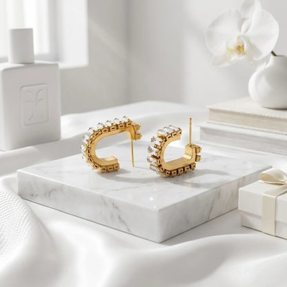 Gold hoop earrings on a marble surface with a white orchid and gift box in the background.