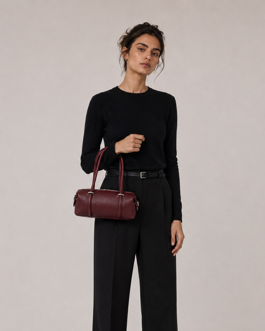Woman holding a burgundy handbag against a plain background