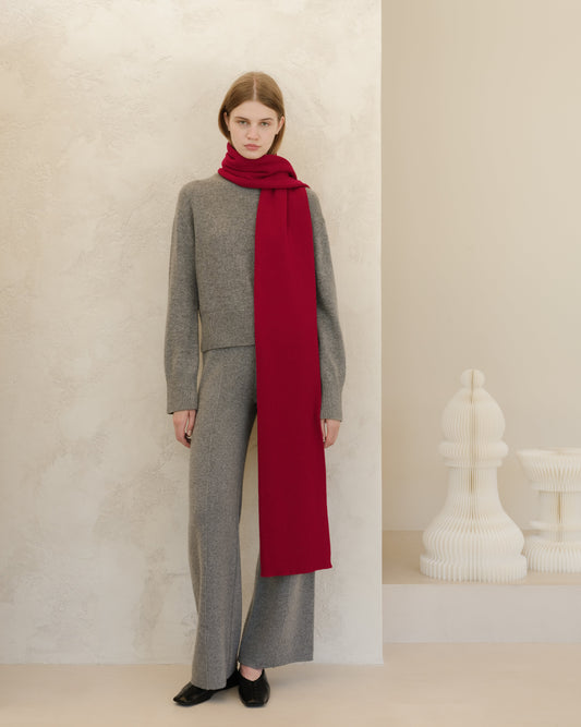 Person wearing a gray outfit with a long red scarf against a neutral background