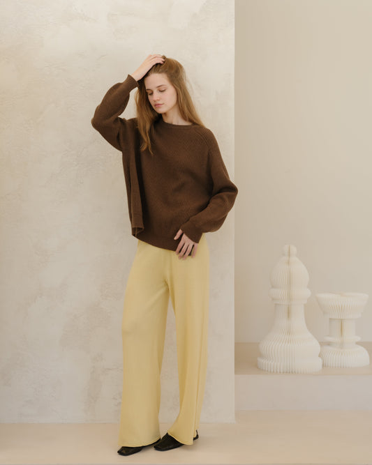 Model wearing a brown ribbed cashmere mix crewneck sweater with side slits and pale yellow wide-leg pants.