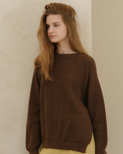 Close-up of a model in a brown ribbed knit sweater with a relaxed fit and pale yellow pants.