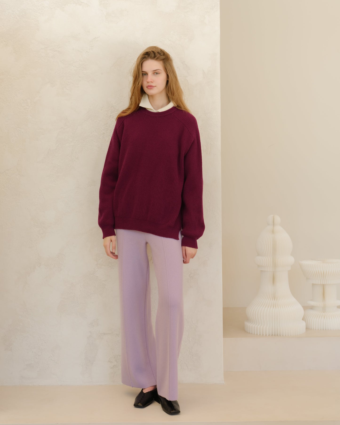 Model wearing burgundy oversized ribbed cashmere mix sweater with a white collared shirt peeking out and lavender trousers.