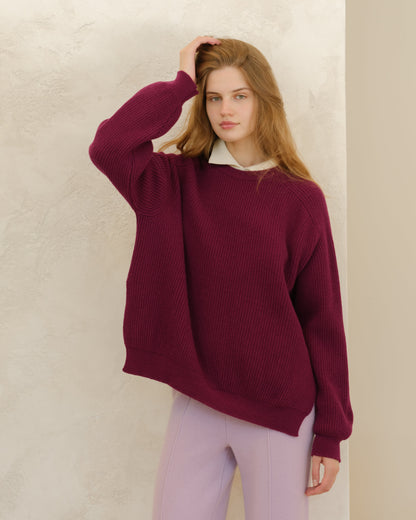 Model wearing burgundy cashmere mix crewneck ribbed sweater with side slits against a textured beige wall.
