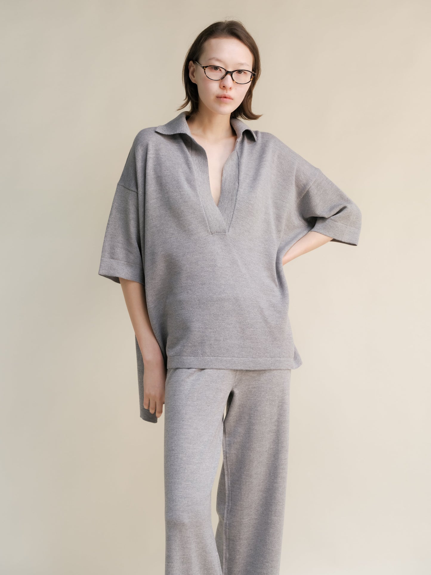 Woman in oversized light gray merino wool maxi polo with deep V-neck and matching wide-leg pants.