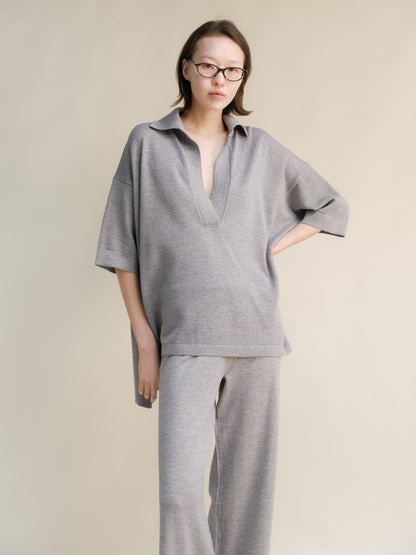 Woman in oversized light gray merino wool maxi polo with deep V-neck and matching wide-leg pants.