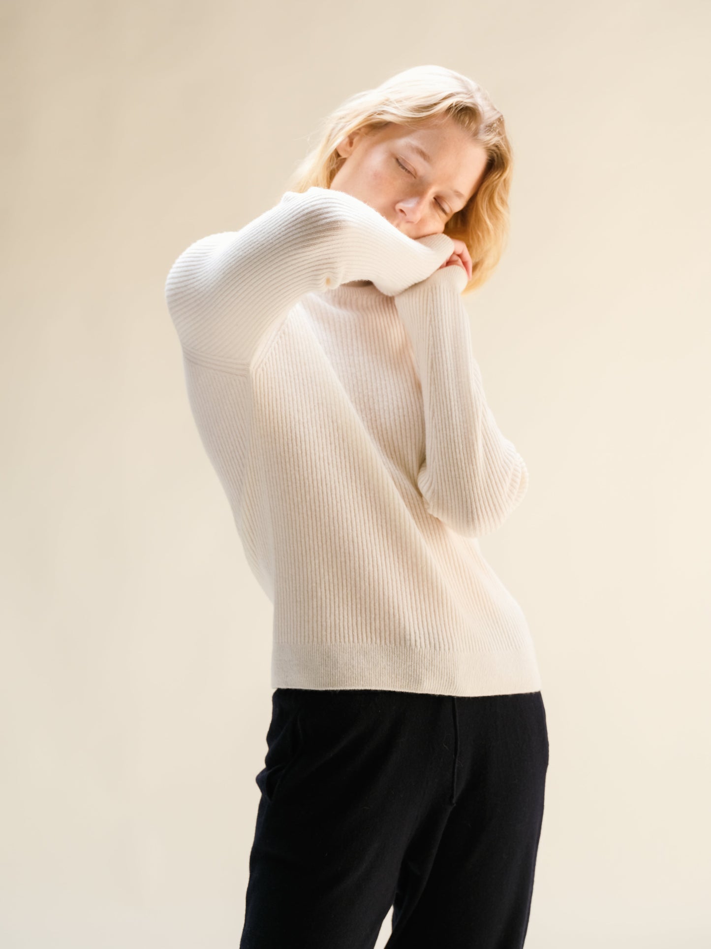 Woman in white ribbed cashmere mix mock neck sweater, back view with arms raised.