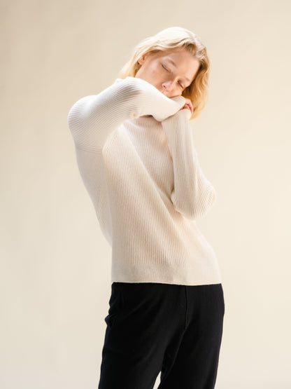 Woman in white ribbed cashmere mix mock neck sweater, back view with arms raised.