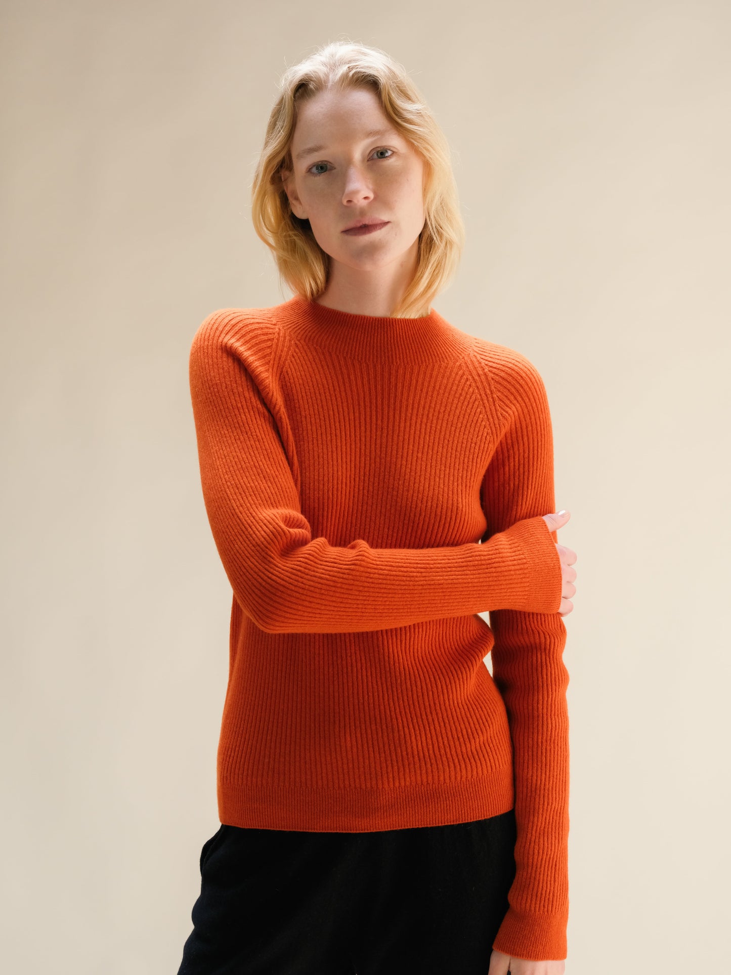 Model wearing a bright orange ribbed cashmere mix mock neck sweater.