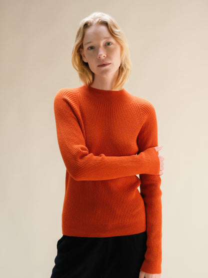 Model wearing a bright orange ribbed cashmere mix mock neck sweater.