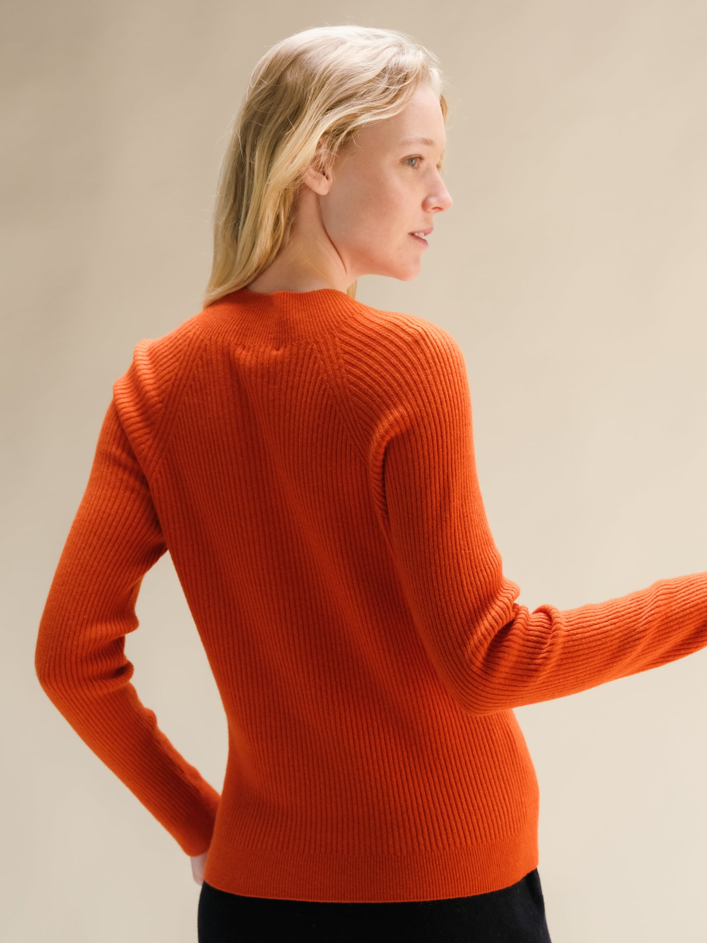 Back view of a bright orange ribbed cashmere mix mock neck sweater on a model.