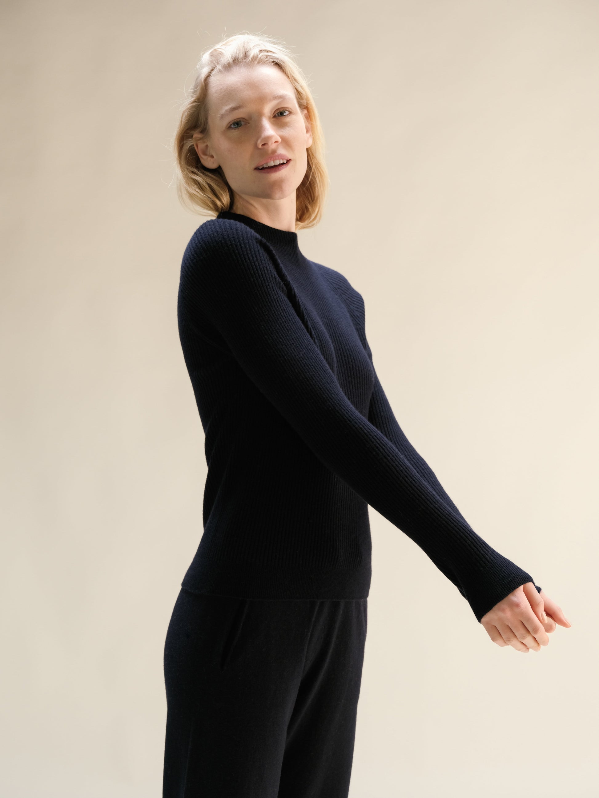 Model wearing navy cashmere mix ribbed mock neck sweater in a relaxed pose with 3D knit texture.