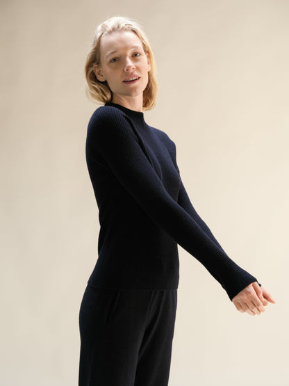 Model wearing navy cashmere mix ribbed mock neck sweater in a relaxed pose with 3D knit texture.
