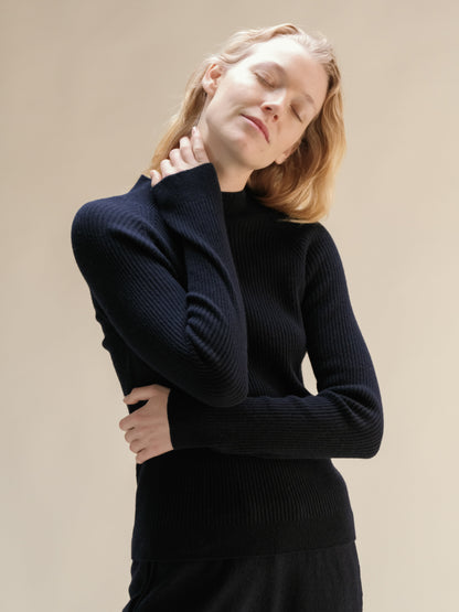 Model in navy cashmere mix ribbed mock neck sweater posing with eyes closed highlighting the soft knit.