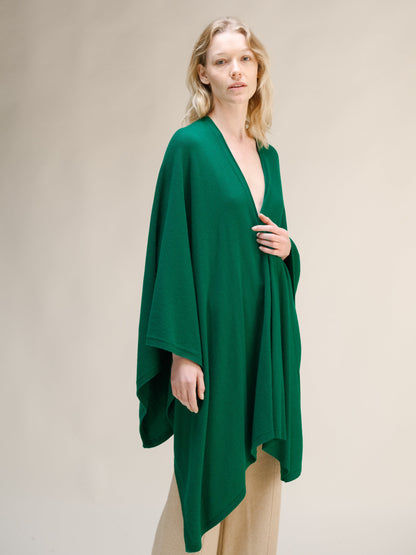 Model wearing emerald green cashmere mix maxi cape with a wrapped front over beige trousers.