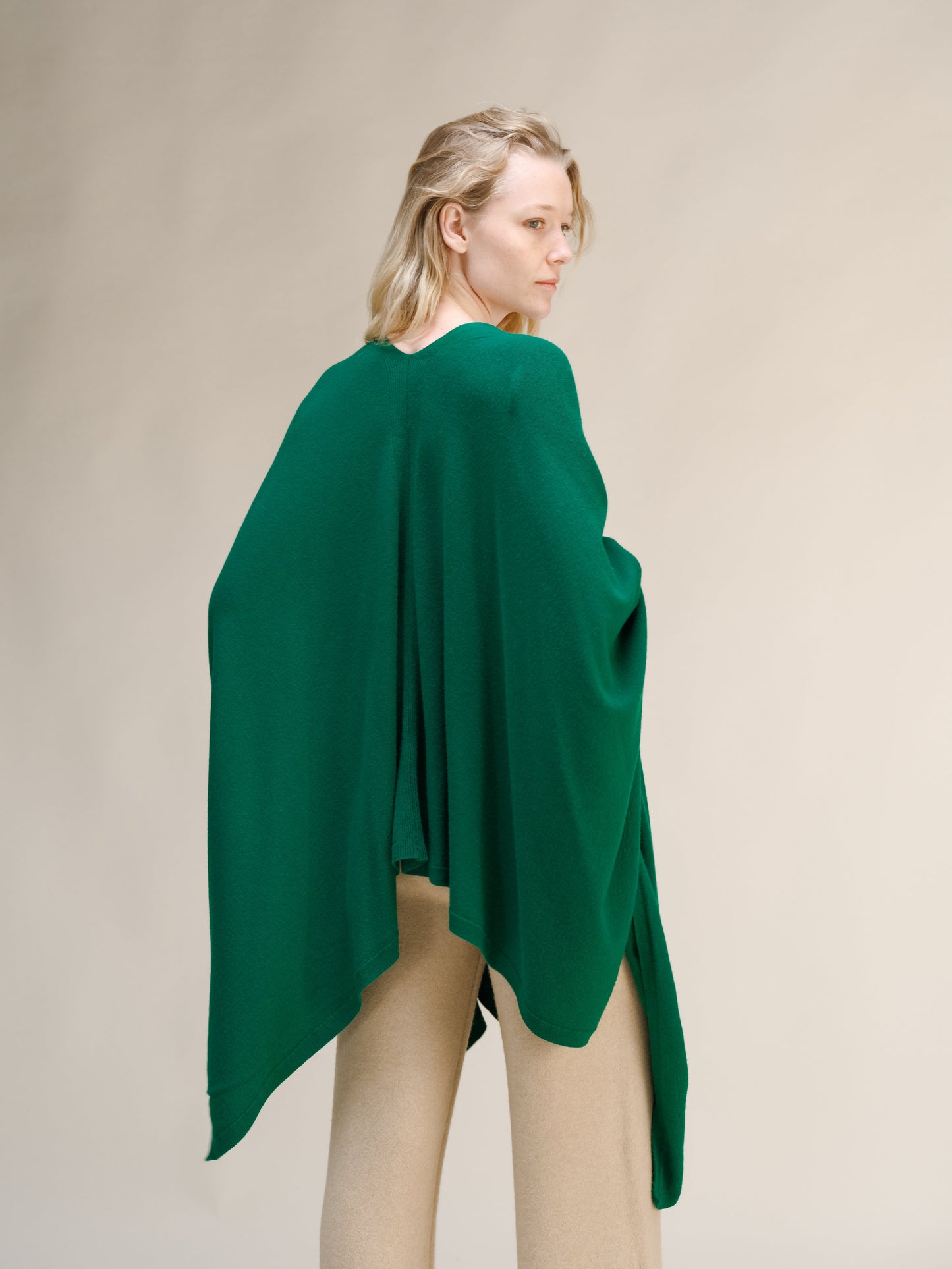 Back view of a model wearing a green cashmere mix maxi cape draped over shoulders with beige pants