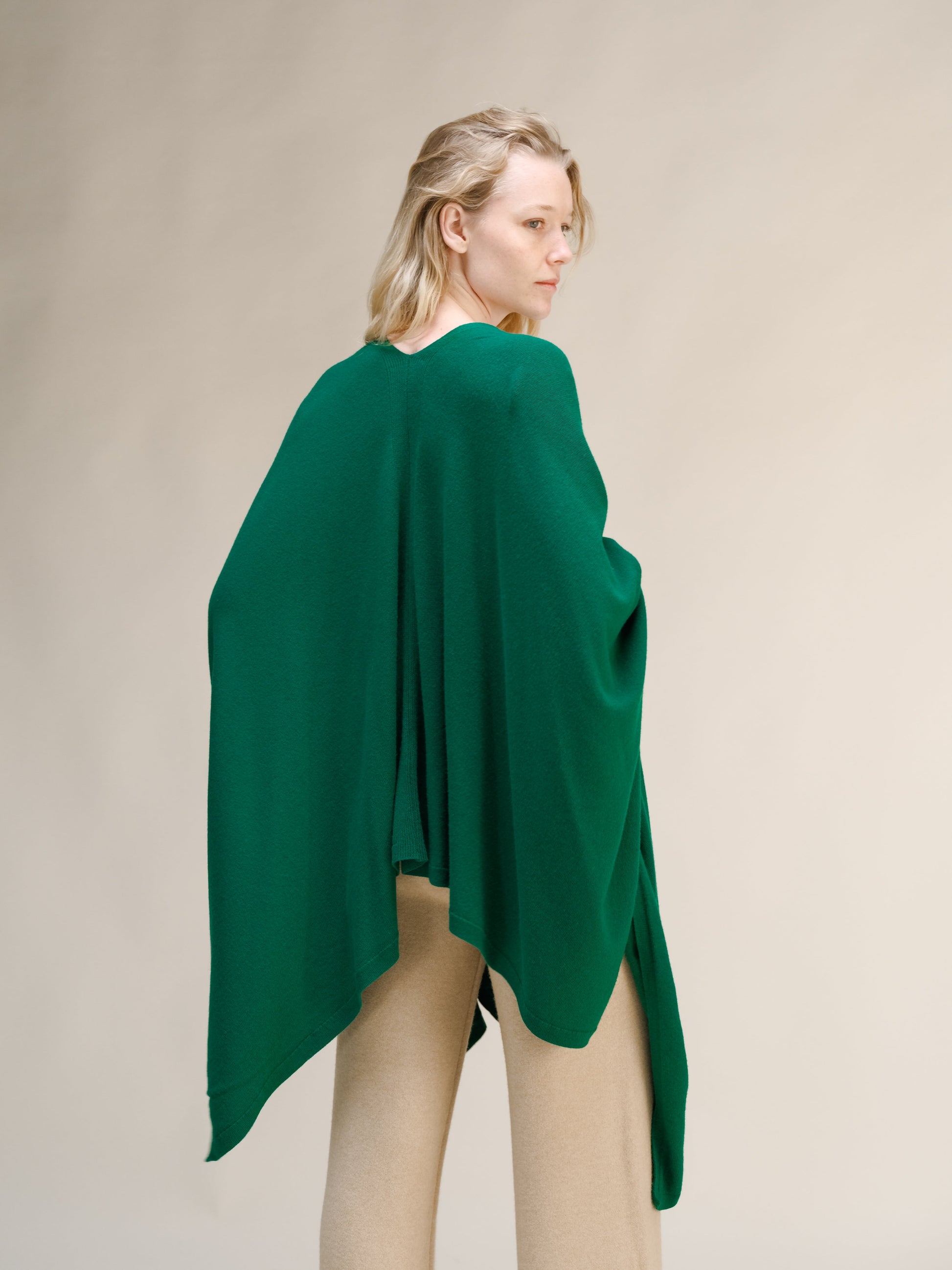 Back view of a model wearing a green cashmere mix maxi cape draped over shoulders with beige pants