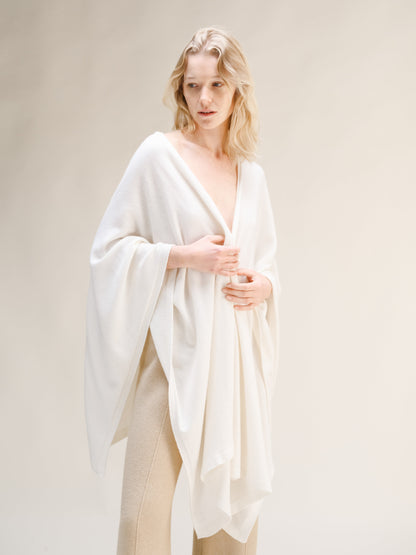 Model wearing a white cashmere mix maxi cape draped over shoulders with beige knit trousers.