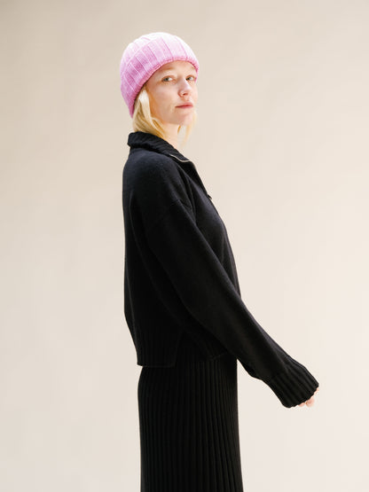 Person wearing a black outfit and pink beanie against a beige background