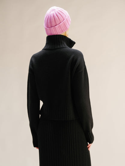 Person wearing a black outfit and pink beanie against a beige background