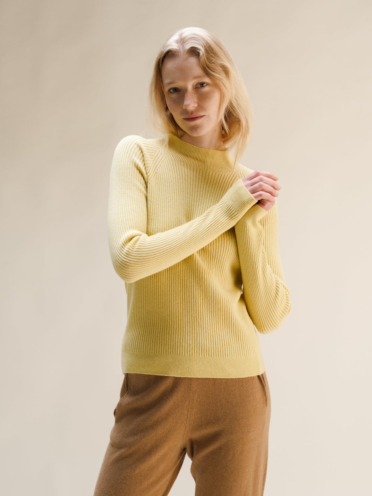 Model wearing a pale yellow ribbed cashmere mix mock neck sweater with tan wide leg pants