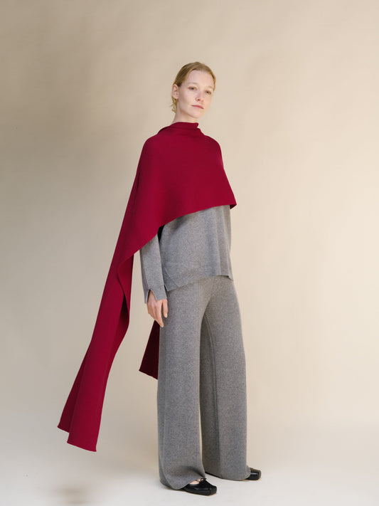 Person wearing a wide red cashmere scarf over a gray outfit on a beige background