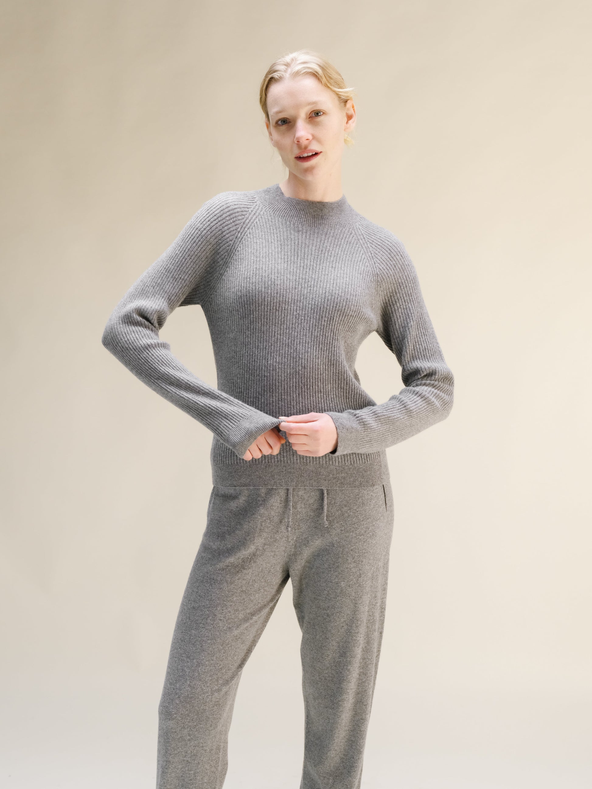 Model wearing gray ribbed cashmere mix mock neck sweater, front view, hands at waist.