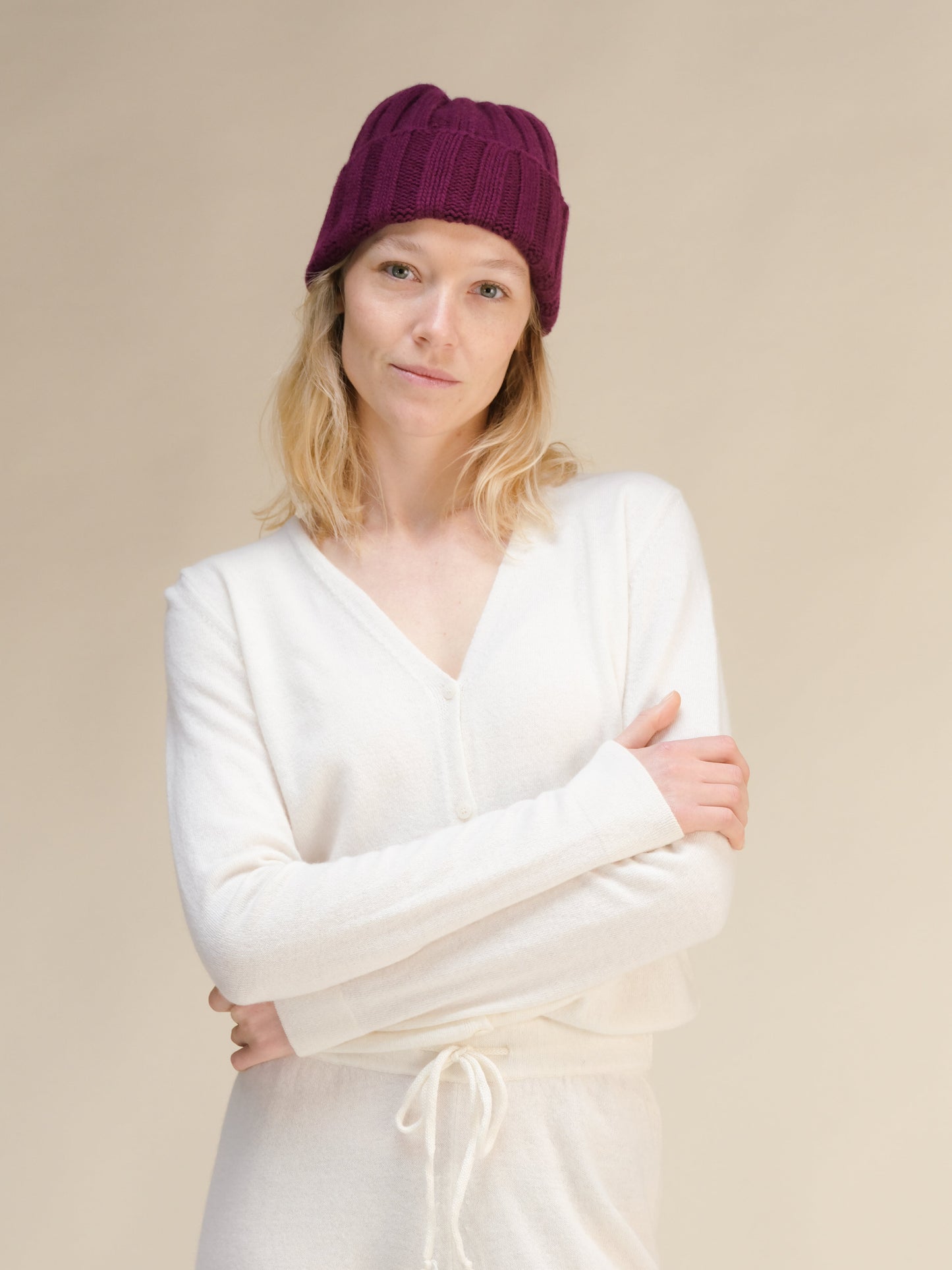 Woman wearing a white sweater and burgundy beanie against a beige background