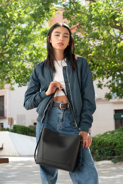 Woman holding a black bag outdoors with greenery in the background