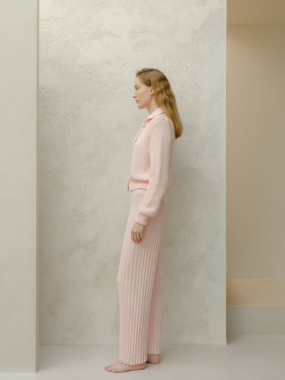 Side view of a model in a pale pink knit set with a sweater and ribbed wide-leg pants against a textured pale wall