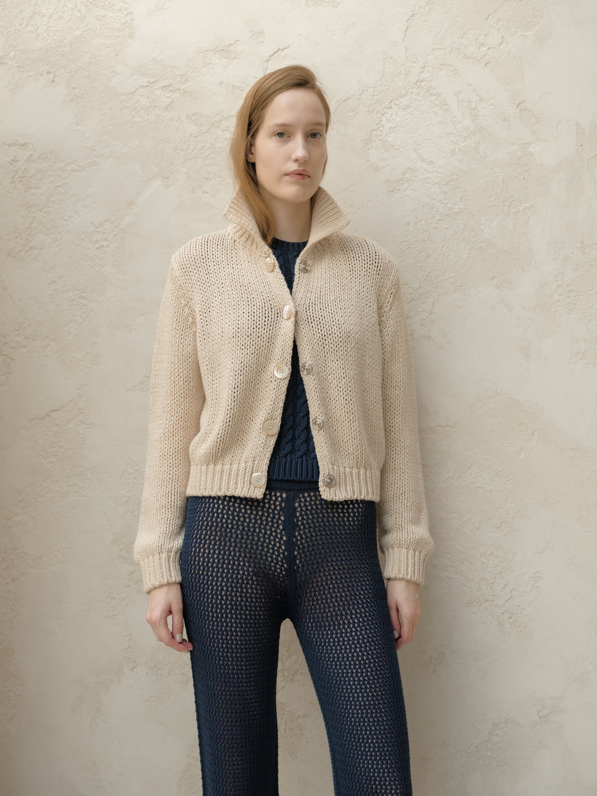 Beige chunky knit bomber jacket with large buttons and a high collar worn by model facing forward