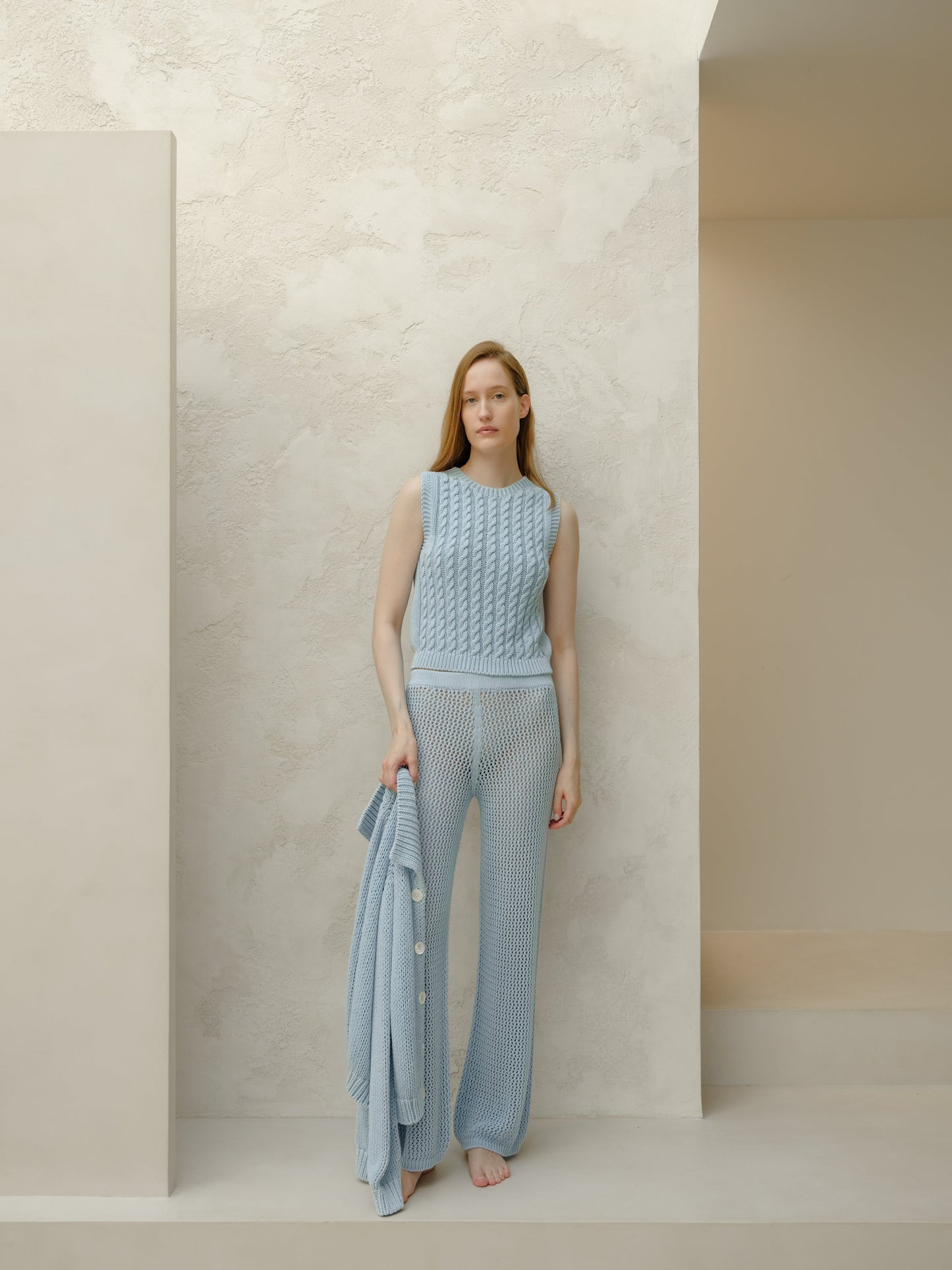 Model in pale blue sleeveless knit top with matching wide leg knit pants holding a cardigan